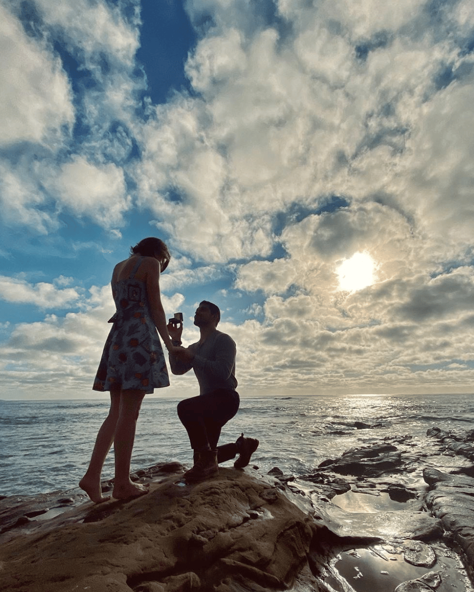 Man proposing to woman on beach with ocean and cloudy sky in background