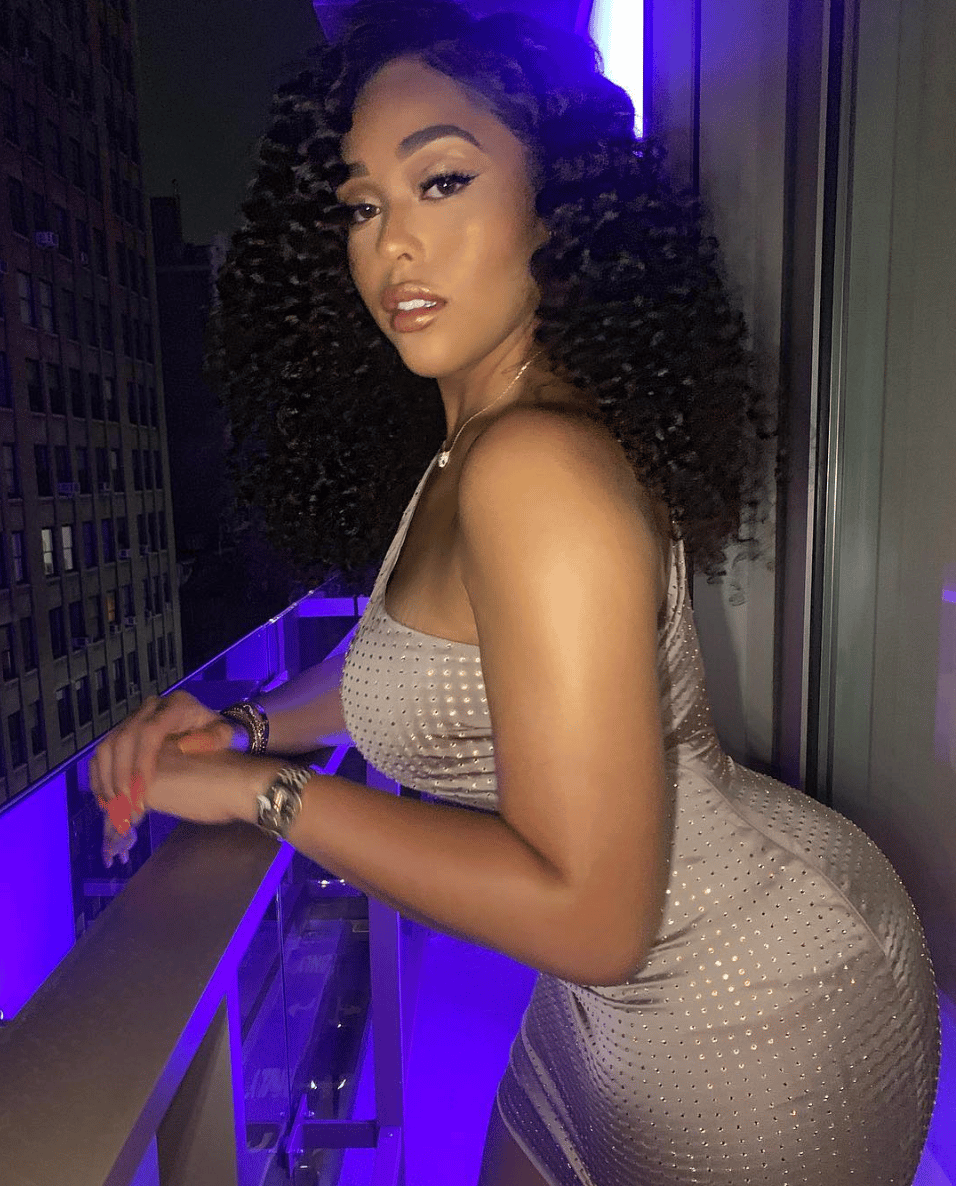 Jordyn Woods posing in a sparkly silver dress at a nightclub with purple lighting