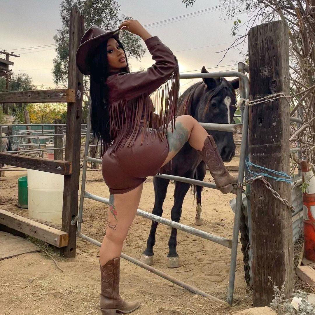 Woman in burgundy fringe jacket and cowboy hat posing at a ranch with a horse