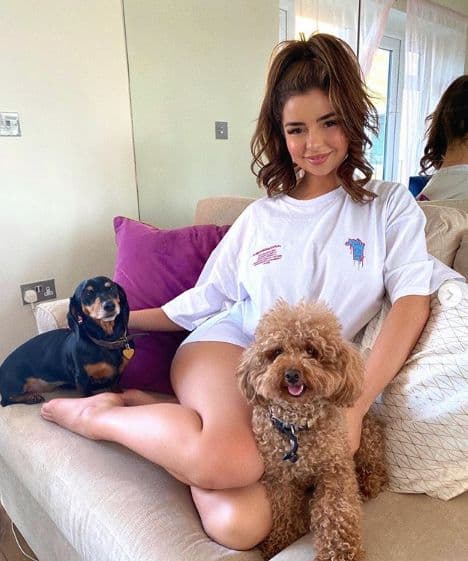 Demi Rose sitting on a bed with two dogs