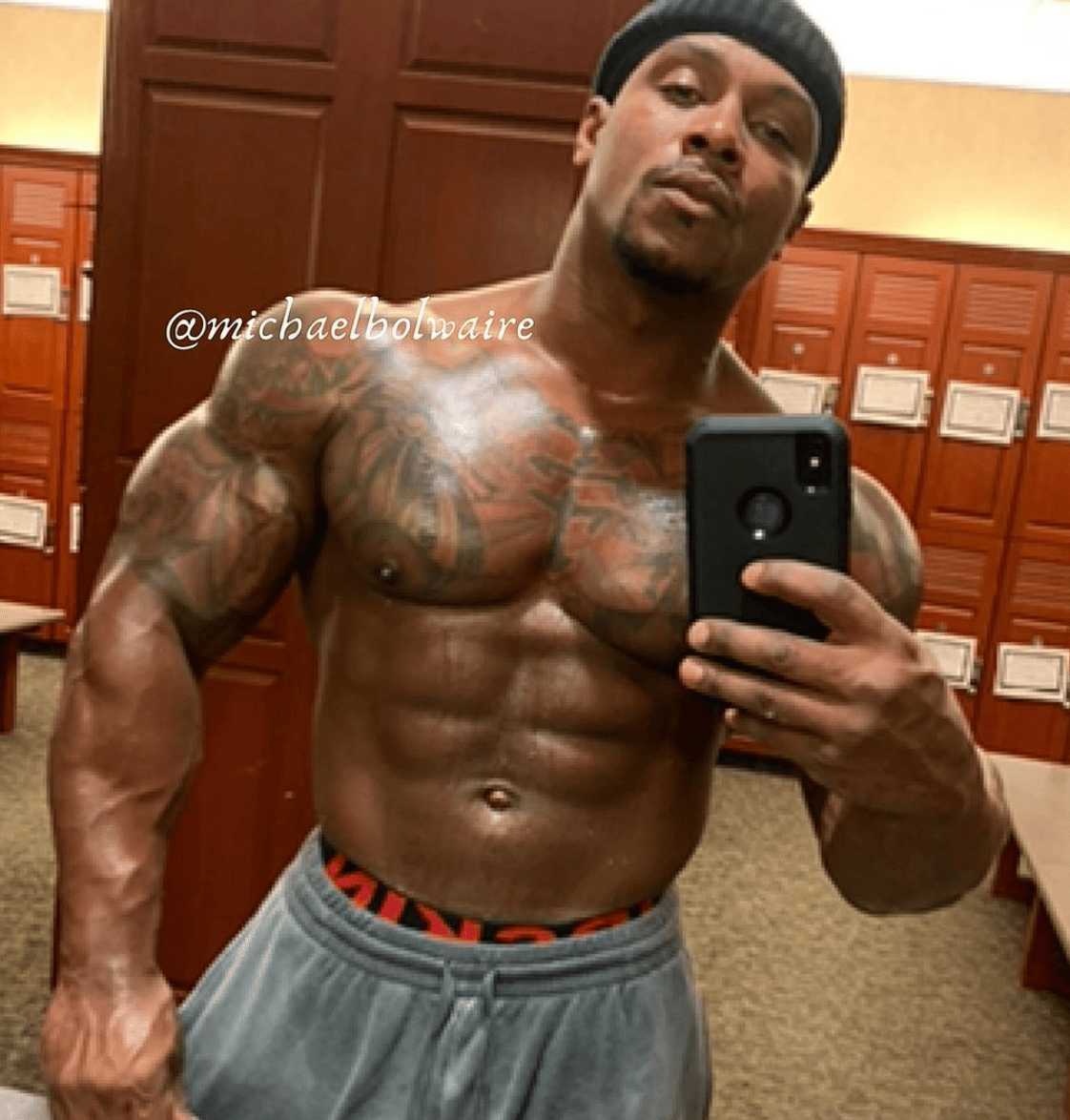 Man taking mirror selfie in locker room, shirtless with visible tattoos