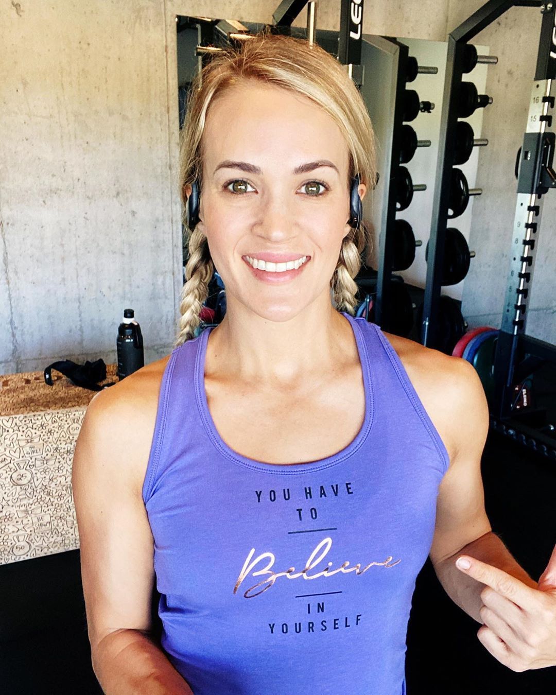 Carrie Underwood in a purple tank top at a gym with weights in the background