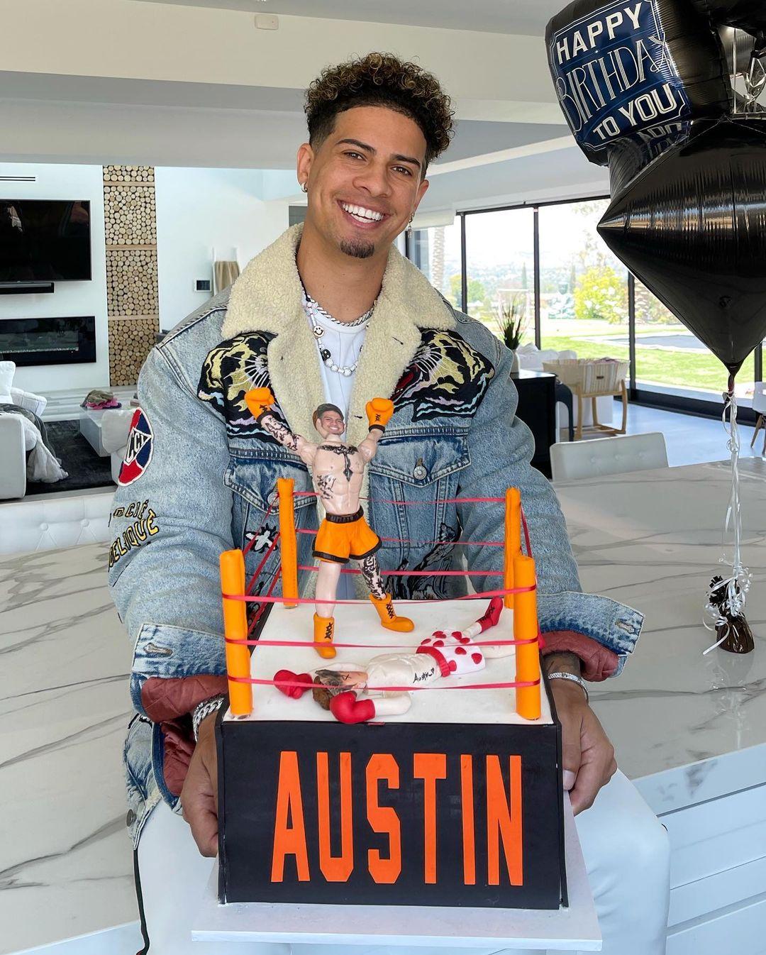 Austin McBroom holds a wrestling ring-themed birthday cake labeled with his name