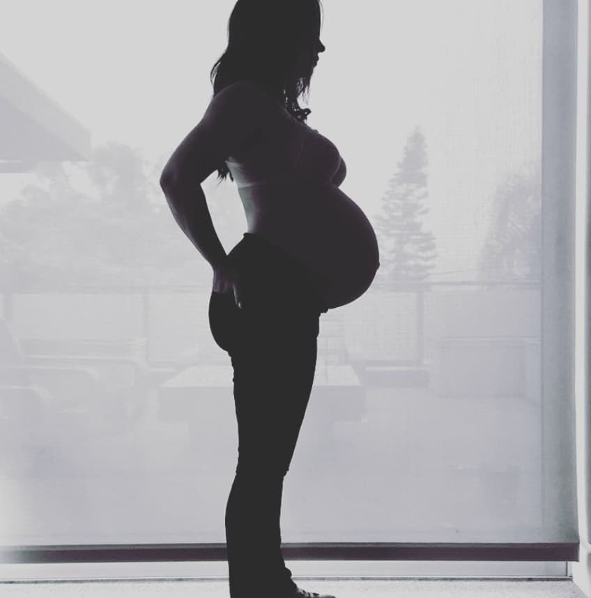 Silhouette of a pregnant woman standing against a window with a city skyline in the background