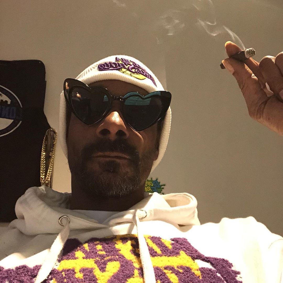 Snoop Dogg wearing heart-shaped sunglasses and a white beanie with purple and yellow design
