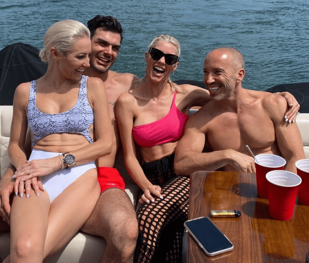 Four people laughing together on a boat with drinks and water in background