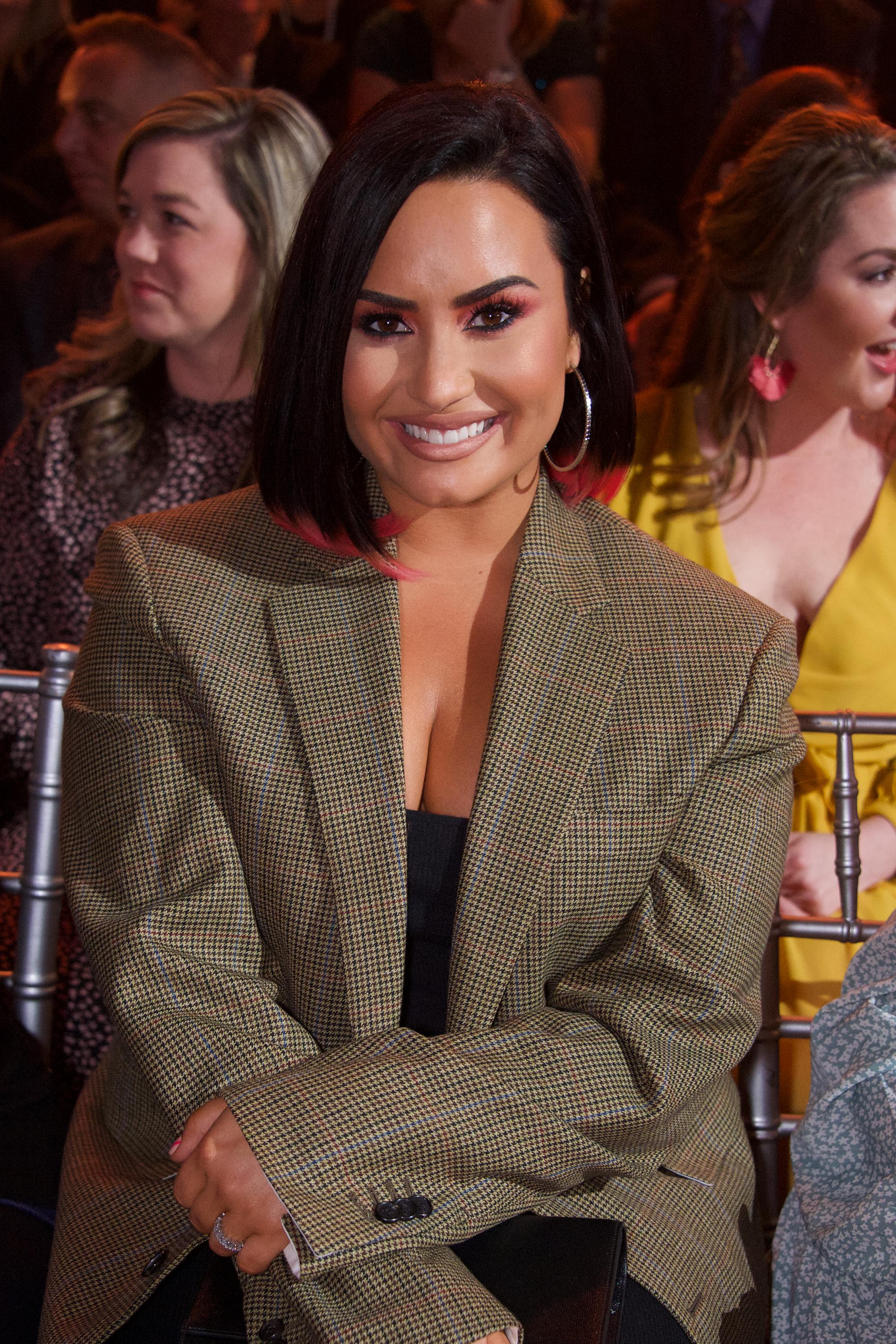 Woman in gold patterned blazer smiling at event with audience in background