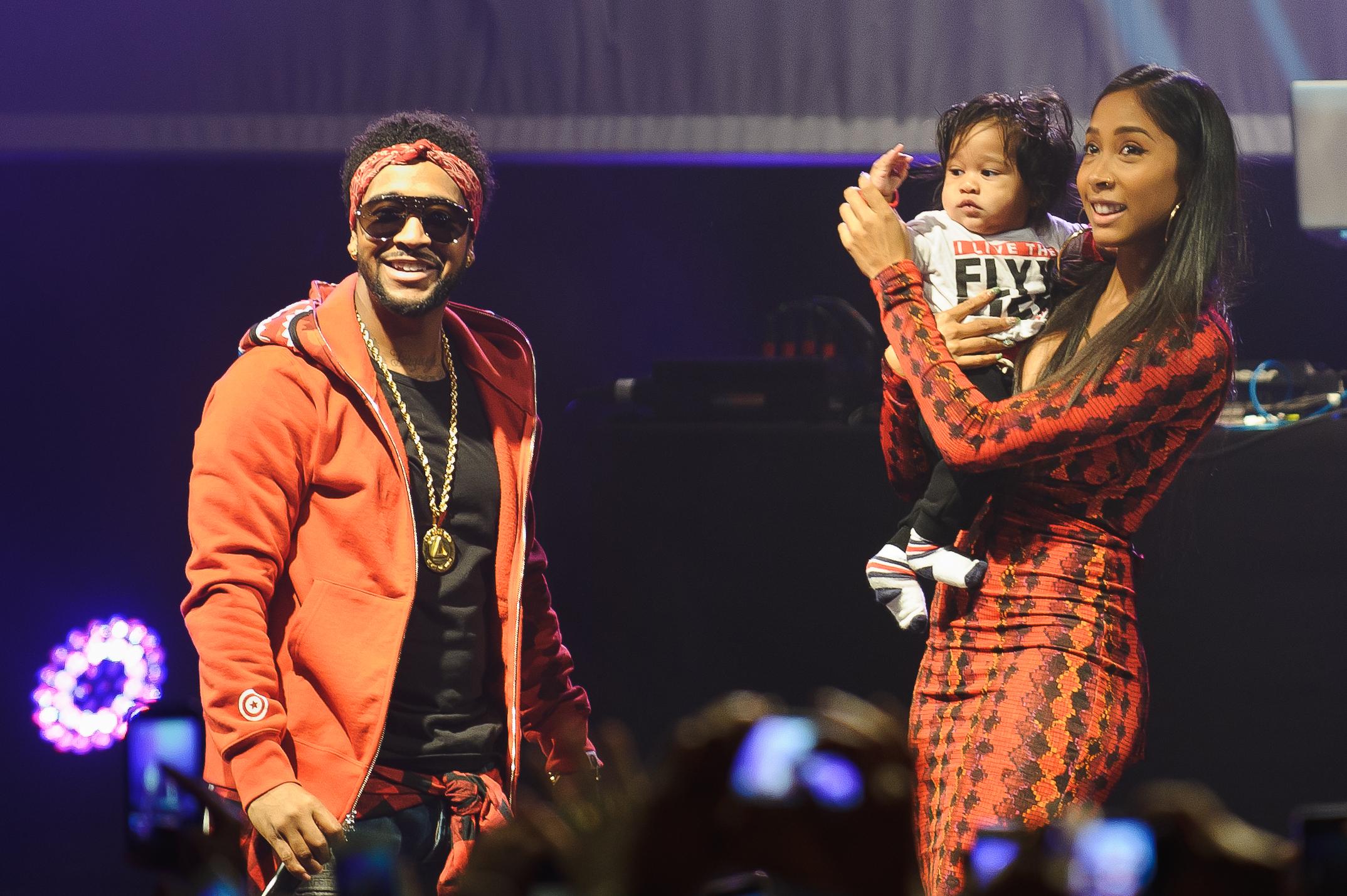 Man in orange blazer and woman in patterned dress holding child on stage at event
