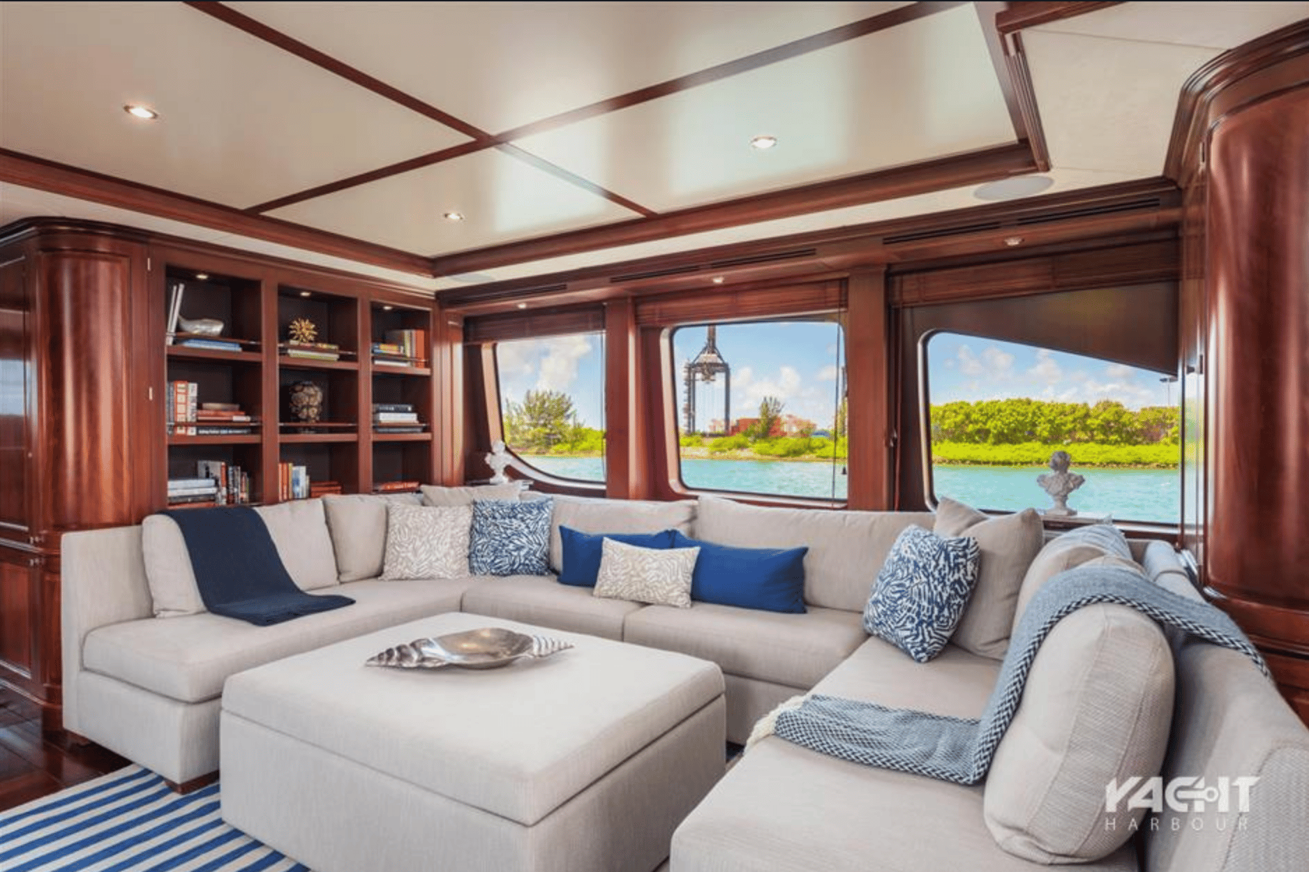 Luxurious yacht lounge with cream sectional sofa, wooden cabinetry, and panoramic water views